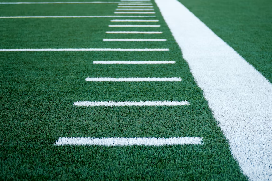 White hashmark lines down the sideline of a green football field. Photo provided by Unsplash.